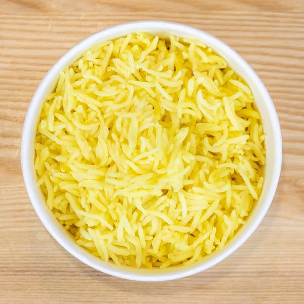 A white bowl filled with bright yellow rice, viewed from directly above on a wooden surface.