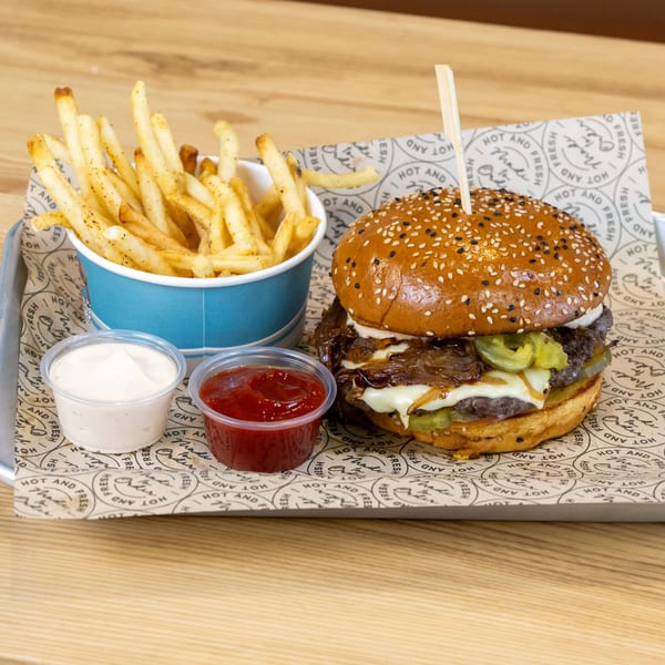Sindbad Burger with caramelized onions, pickles, and cheese, served with fries and dipping sauces.
