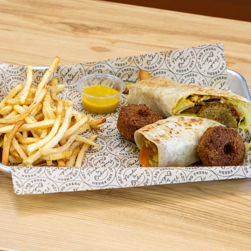Sindbad Burger's falafel wraps, golden fries, and dipping sauce on a branded paper-lined tray.