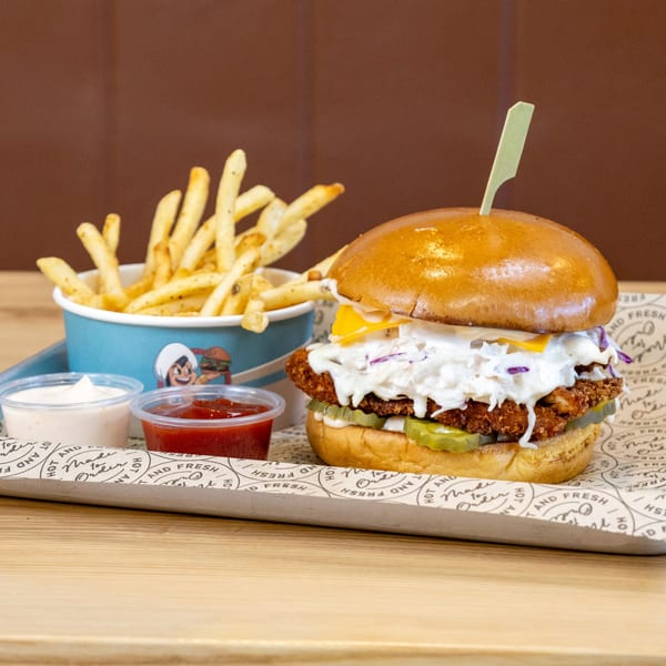 A Sindbad Burger with coleslaw, cheese, and pickles, served with fries, ketchup, and mayonnaise.