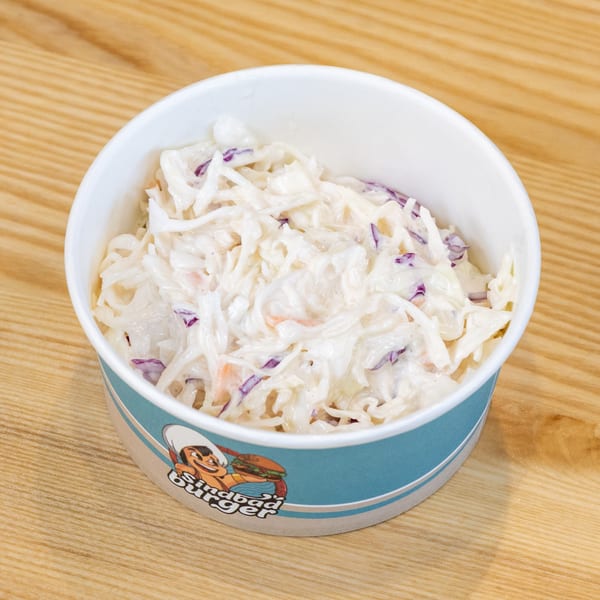 Creamy coleslaw with white and purple cabbage in a Sindbad Burger branded cup on a wooden table.