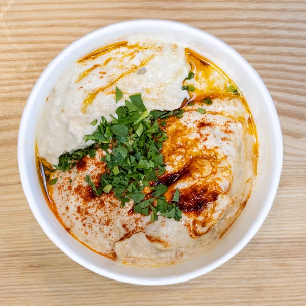Creamy hummus topped with paprika, olive oil, and fresh parsley in a white bowl.