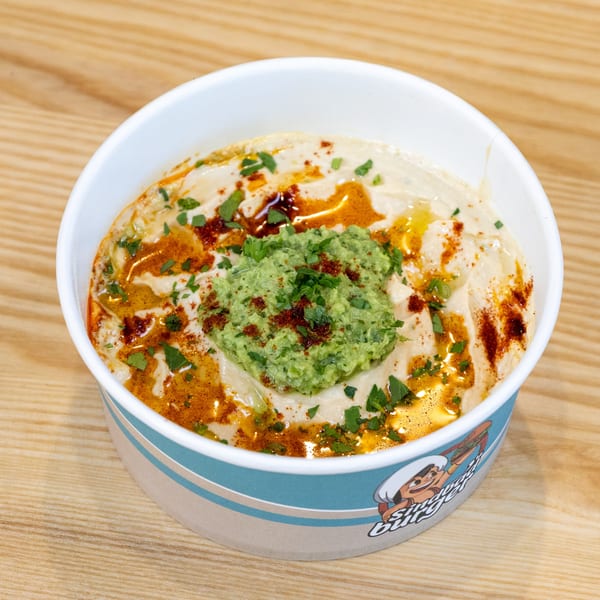 Hummus topped with green relish, paprika, and parsley in a Sindbad Burger branded bowl.