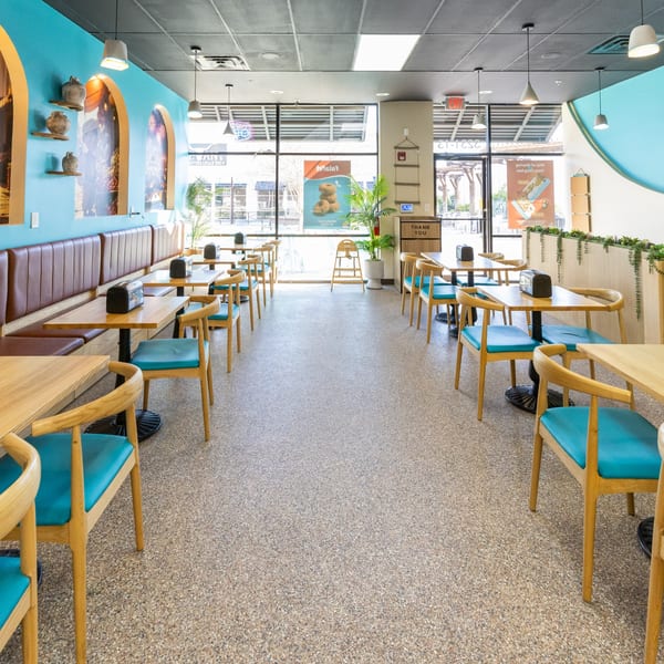 Interior of Sindbad Burger restaurant with turquoise walls, wooden tables, and teal chairs.